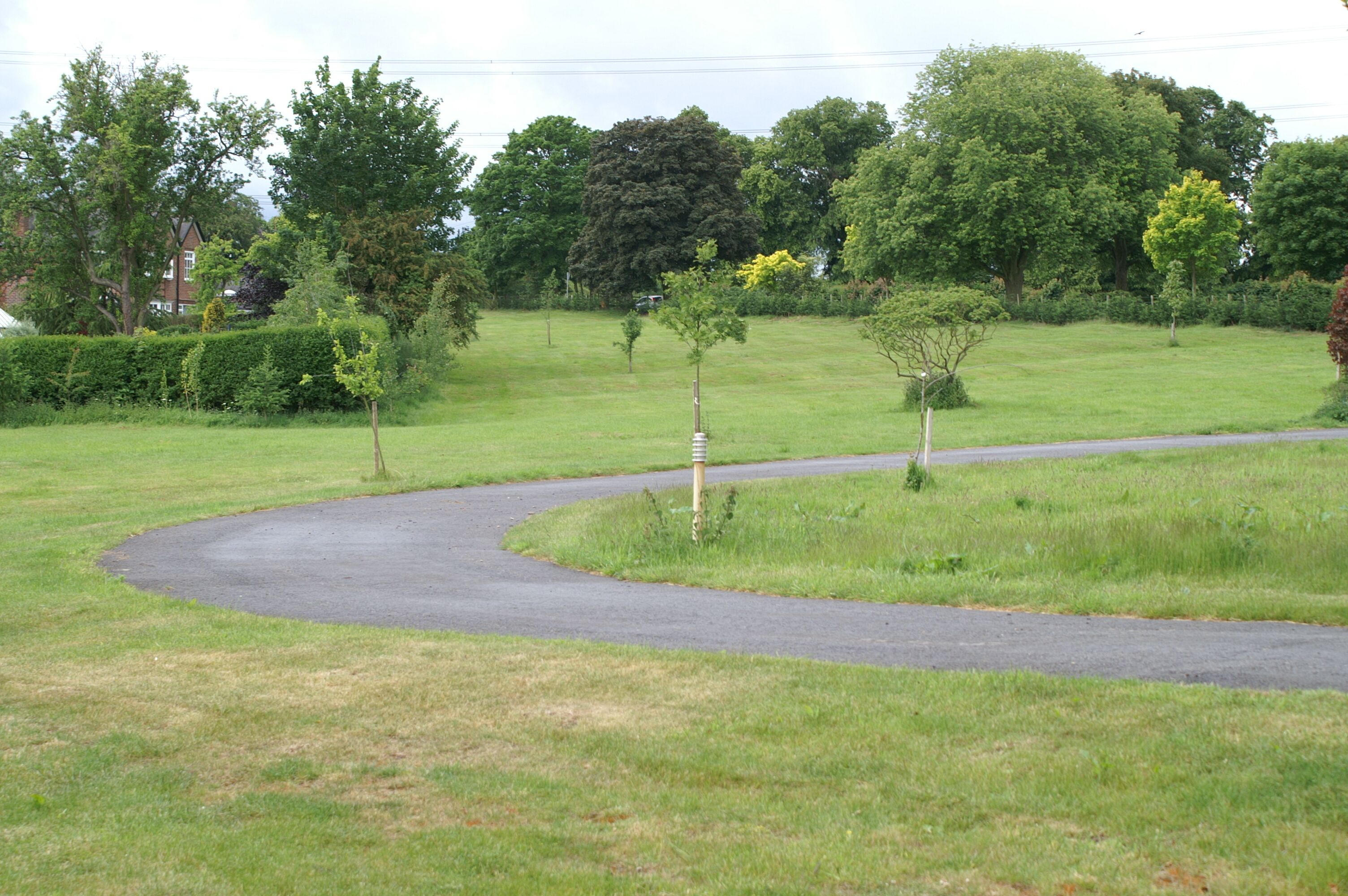 A curved road in a grassy area with trees and a house in the background.