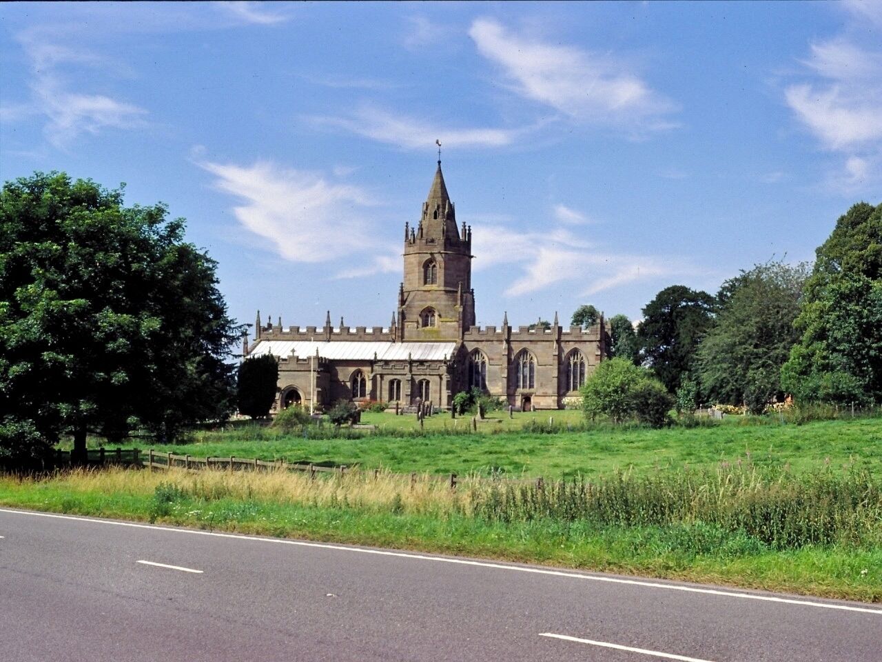 A historic church with a tall tower, surrounded by lush greenery and a clear sky.