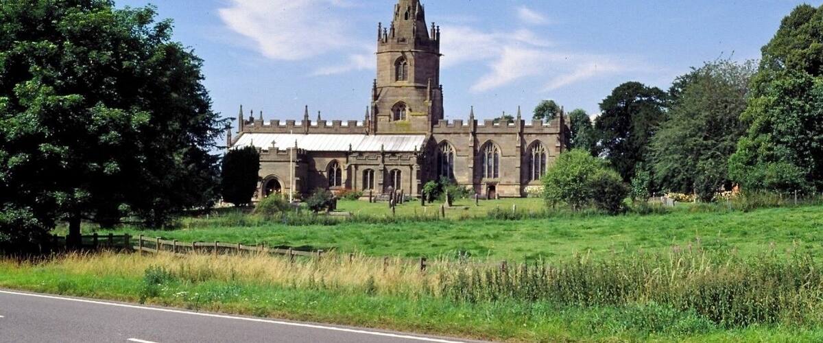 A historic church with a tall tower, surrounded by lush greenery and a clear sky.