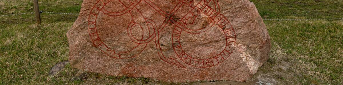A large rock with red carvings in a grassy field.