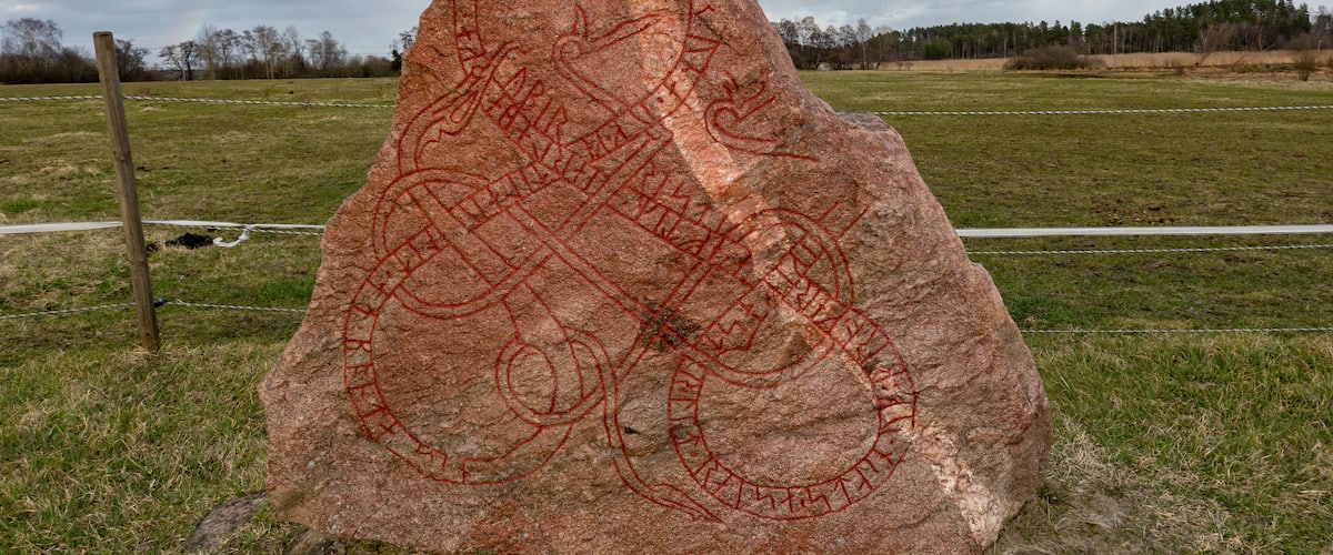 Een grote rots met rode gravures in een grasveld.