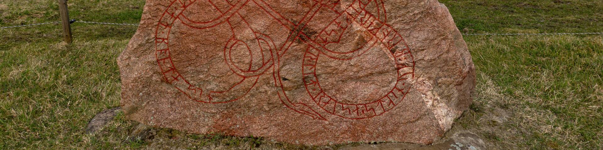 A large rock with red carvings in a grassy field.