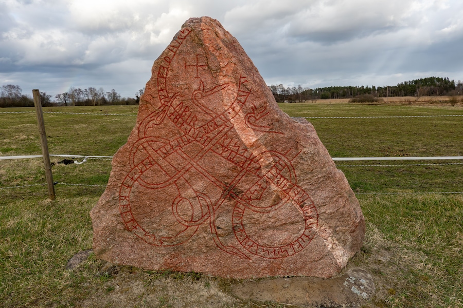 A large rock with red carvings in a grassy field.
