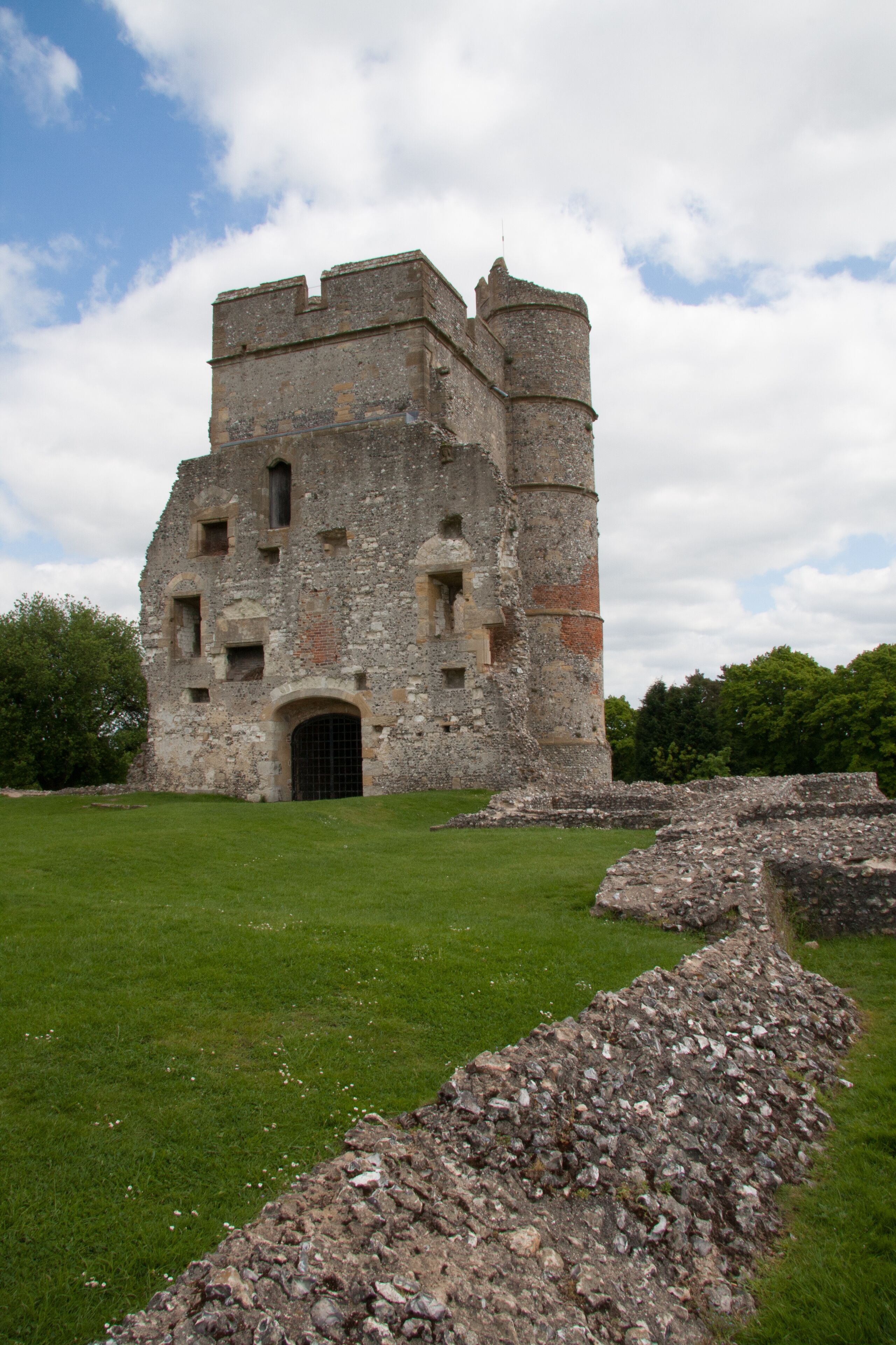 An ancient stone castle with a grassy courtyard and ruins in the foreground.