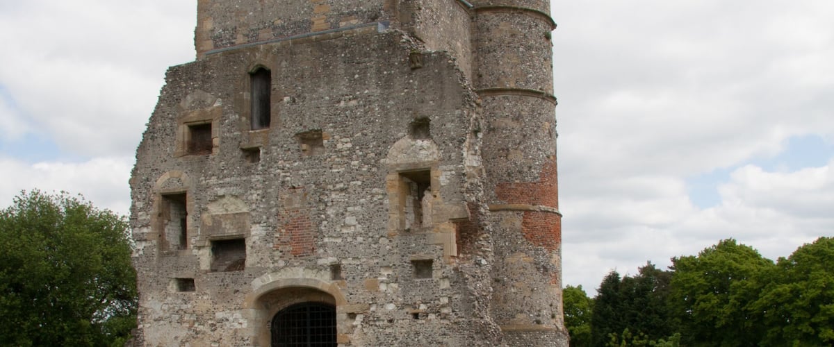 An ancient stone castle with a grassy courtyard and ruins in the foreground.