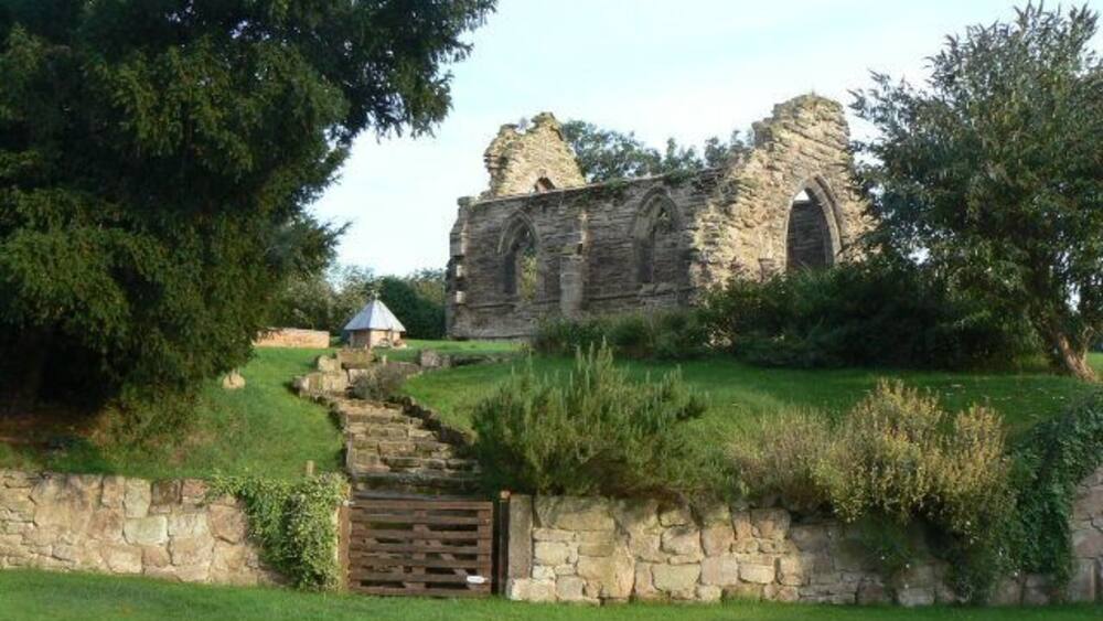 An ancient stone structure with arches, a grassy pathway, and a stone wall.