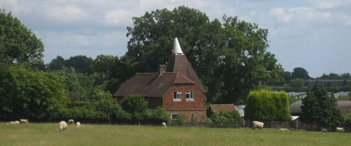 A rural landscape with a brick house, a conical roof, and sheep grazing in the foreground.
