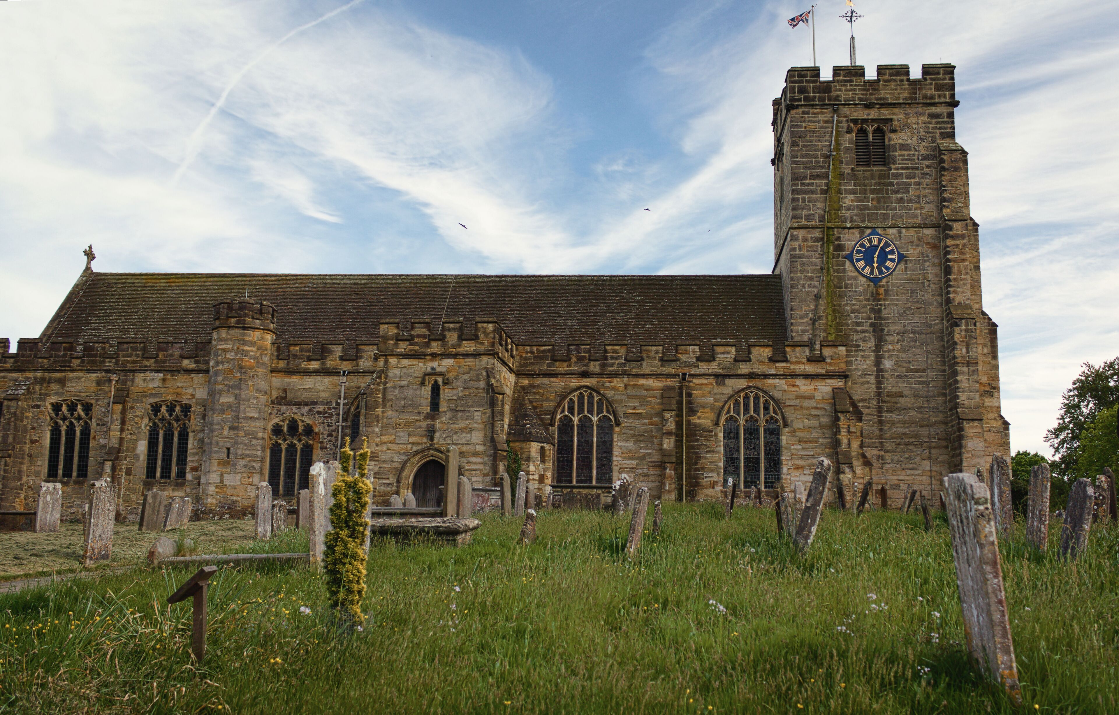 A historic stone church with a clock tower and a graveyard in front.