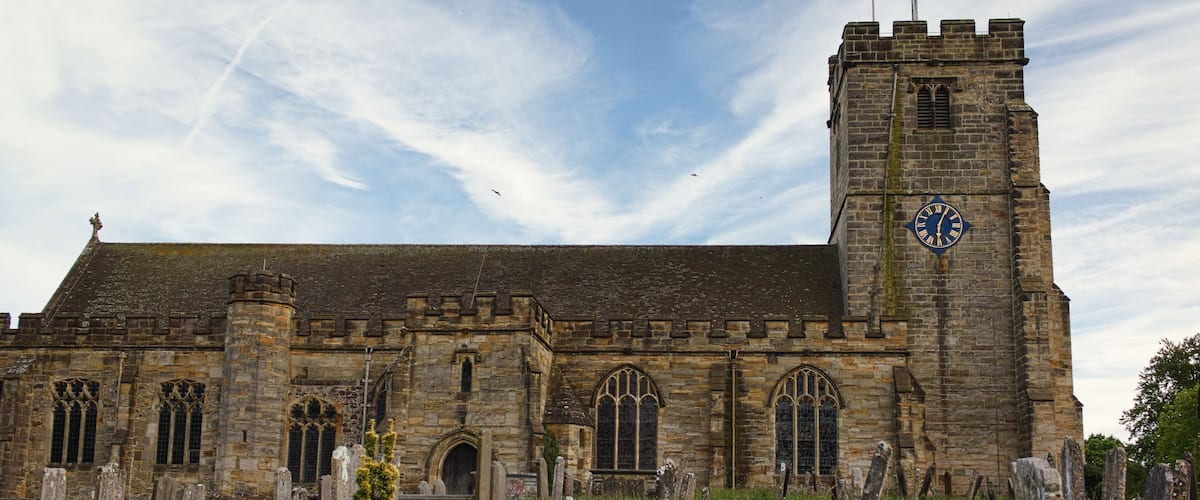 A historic stone church with a clock tower and a graveyard in front.