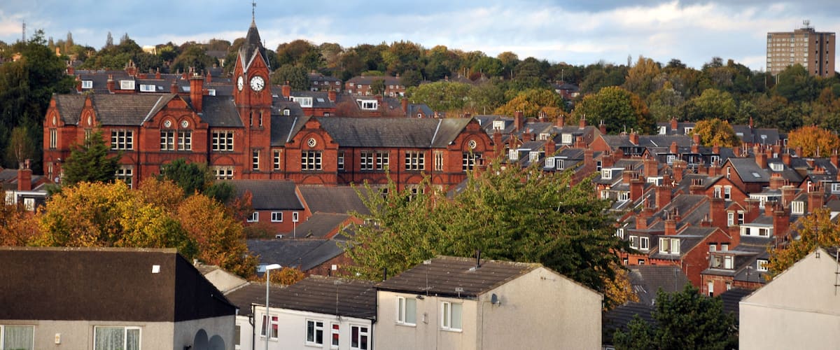 A red-brick building with a clock tower, surrounded by residential houses and autumn foliage.