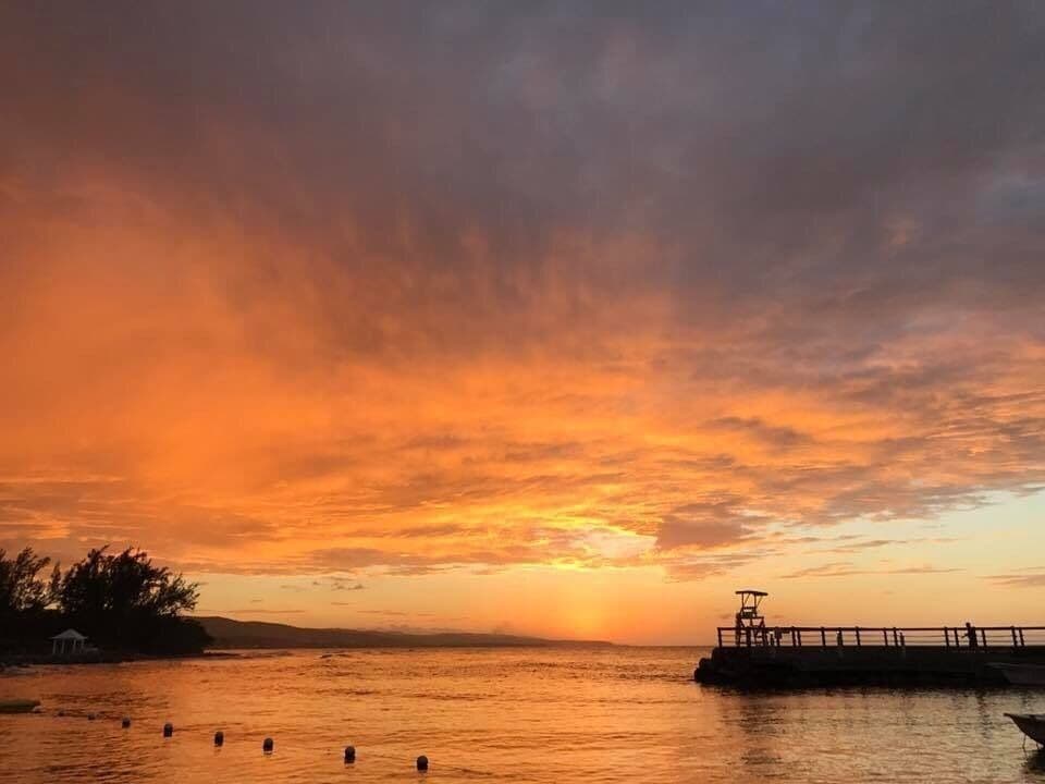 A sunset over a calm body of water with a pier and a gazebo on the left.