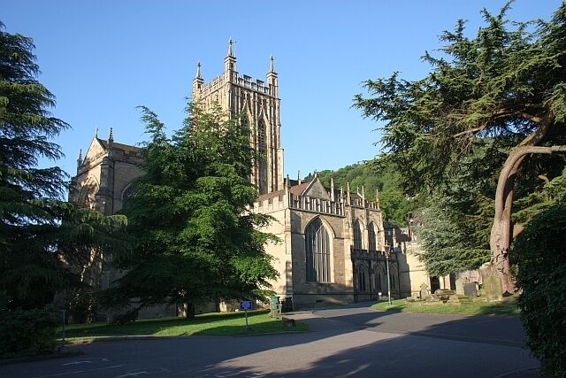 A historic church with tall spires and a large arched entrance, surrounded by trees and a clear sky.