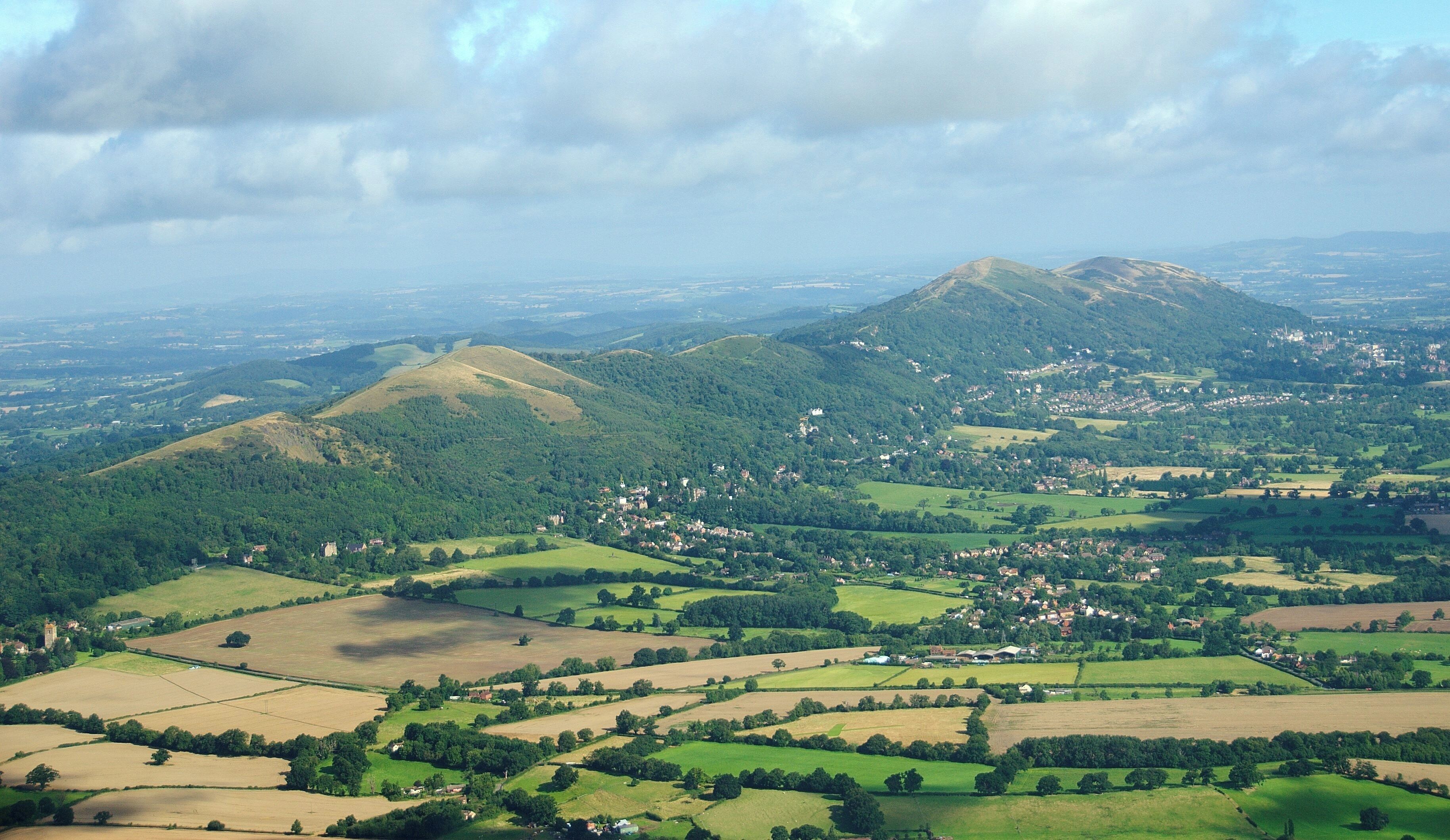 A rural landscape with rolling hills, fields, and scattered houses.