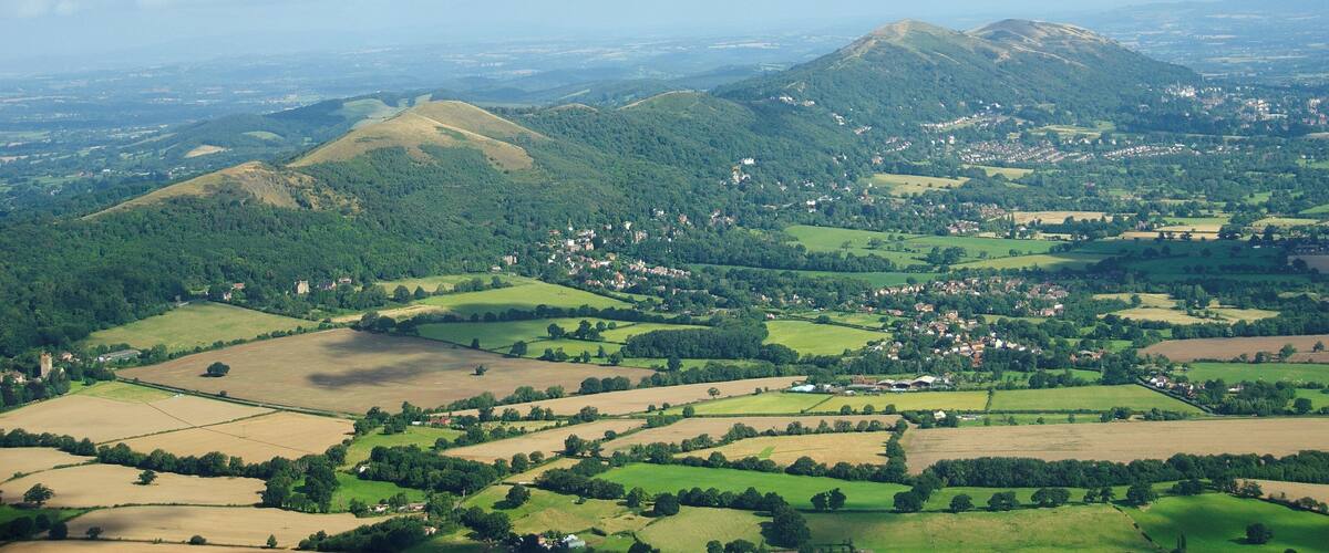 A rural landscape with rolling hills, fields, and scattered houses.
