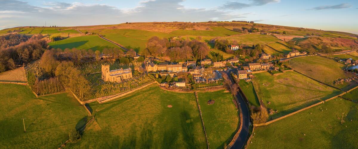 An aerial view of a village with a prominent church, rolling hills, and a river.