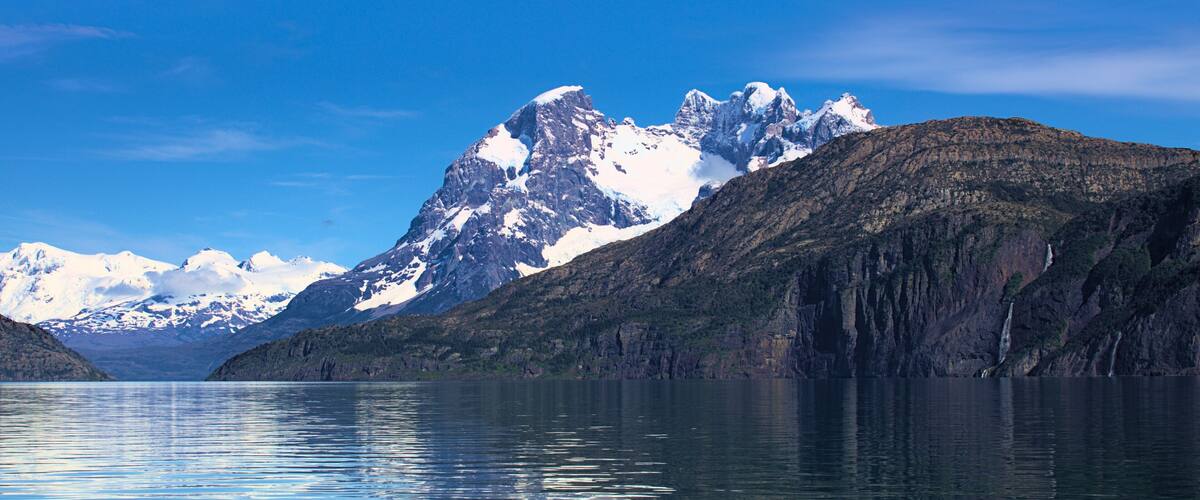 A mountain range with snow-capped peaks and a calm lake reflecting the scenery.