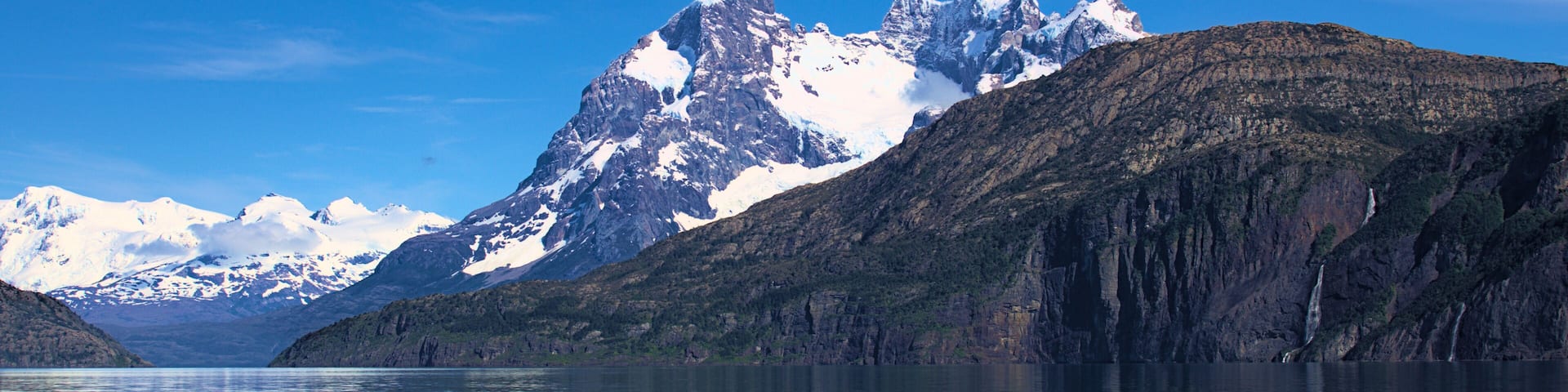 A mountain range with snow-capped peaks and a calm lake reflecting the scenery.
