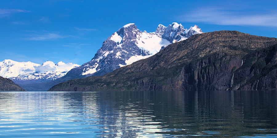 A mountain range with snow-capped peaks and a calm lake reflecting the scenery.