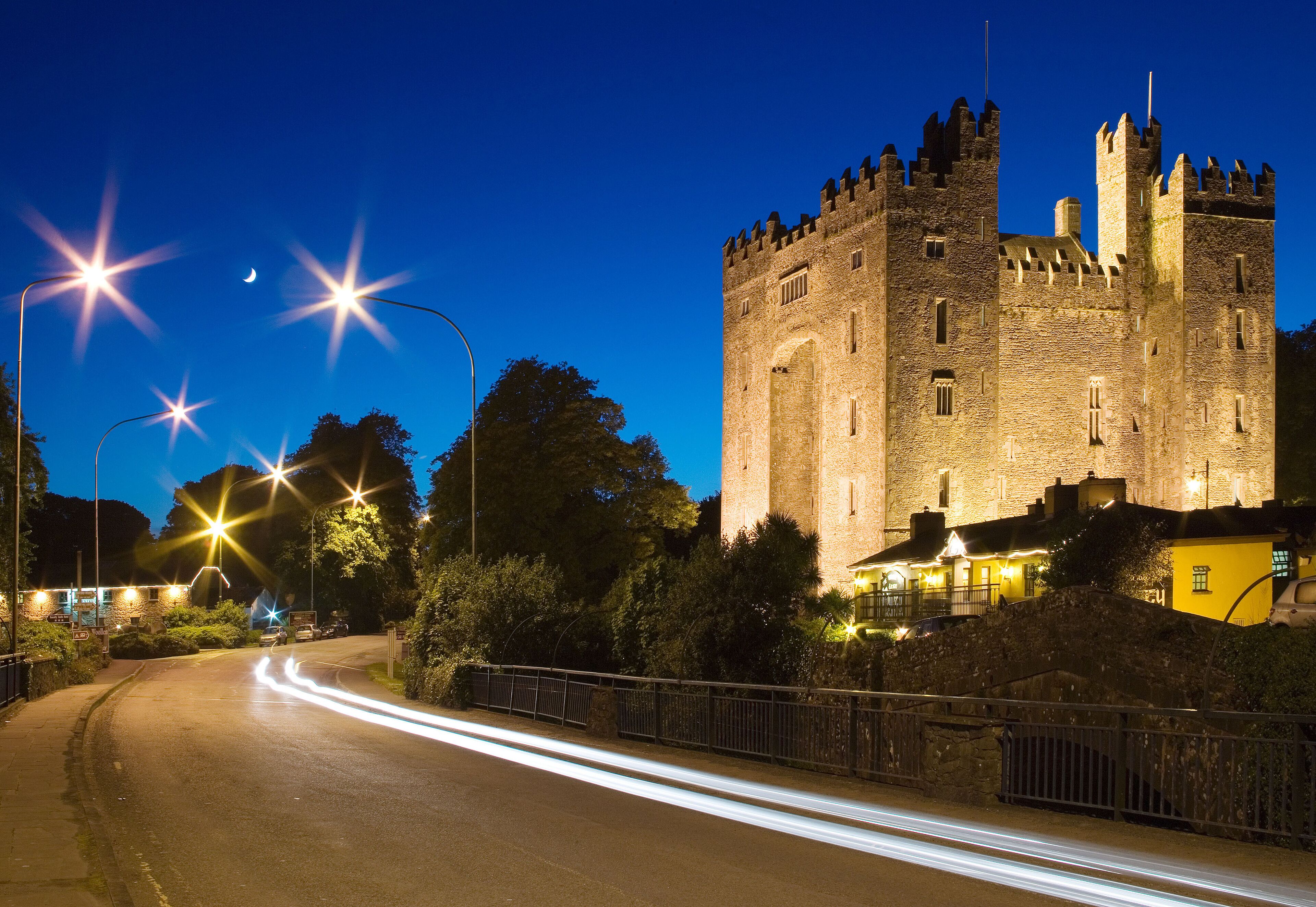 A historic castle at dusk with illuminated windows and a moat.
