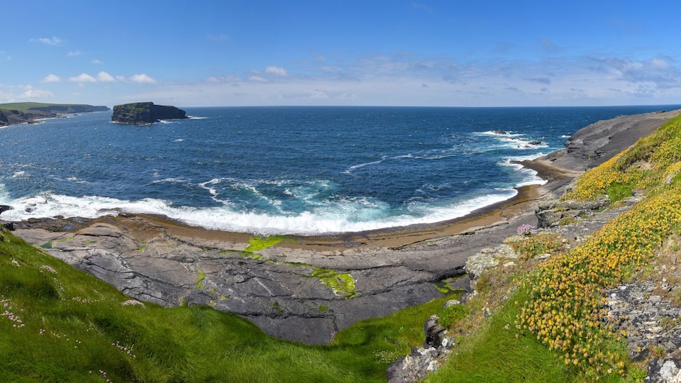A coastal landscape with cliffs, a rocky shoreline, and a clear blue sea.