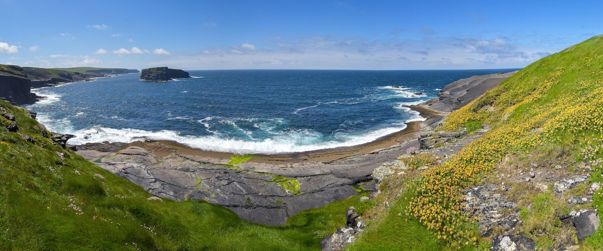 A coastal landscape with cliffs, a rocky shoreline, and a clear blue sea.