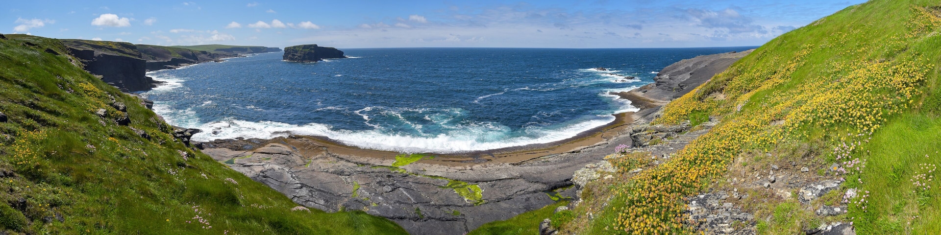 A coastal landscape with cliffs, a rocky shoreline, and a clear blue sea.