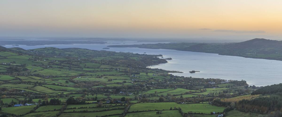 A coastal landscape with rolling green hills, a large body of water, and distant mountains.