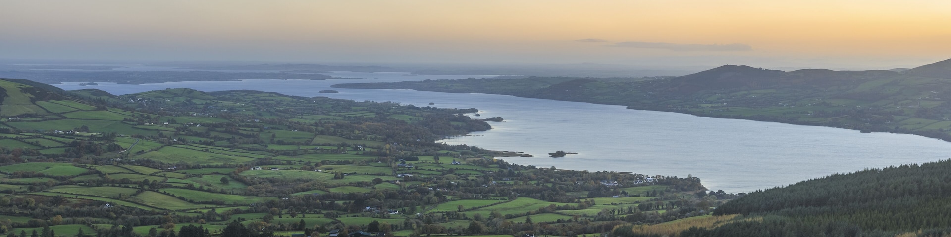 A coastal landscape with rolling green hills, a large body of water, and distant mountains.