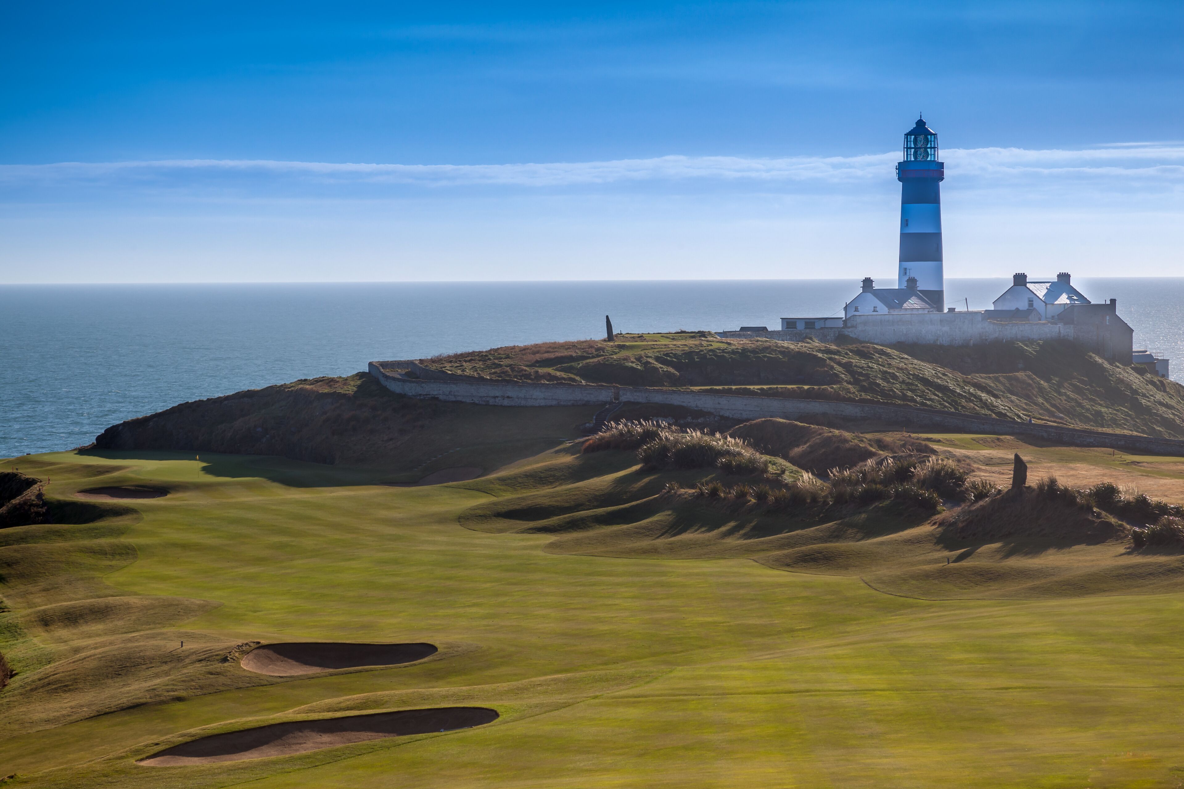 A lighthouse on a grassy hill overlooking the sea.
