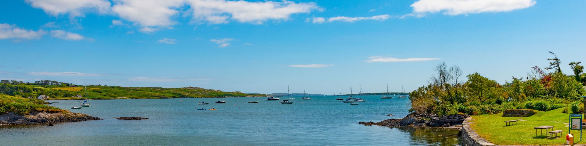 Una bahía tranquila con barcos, una orilla cubierta de hierba y un muro de piedra.