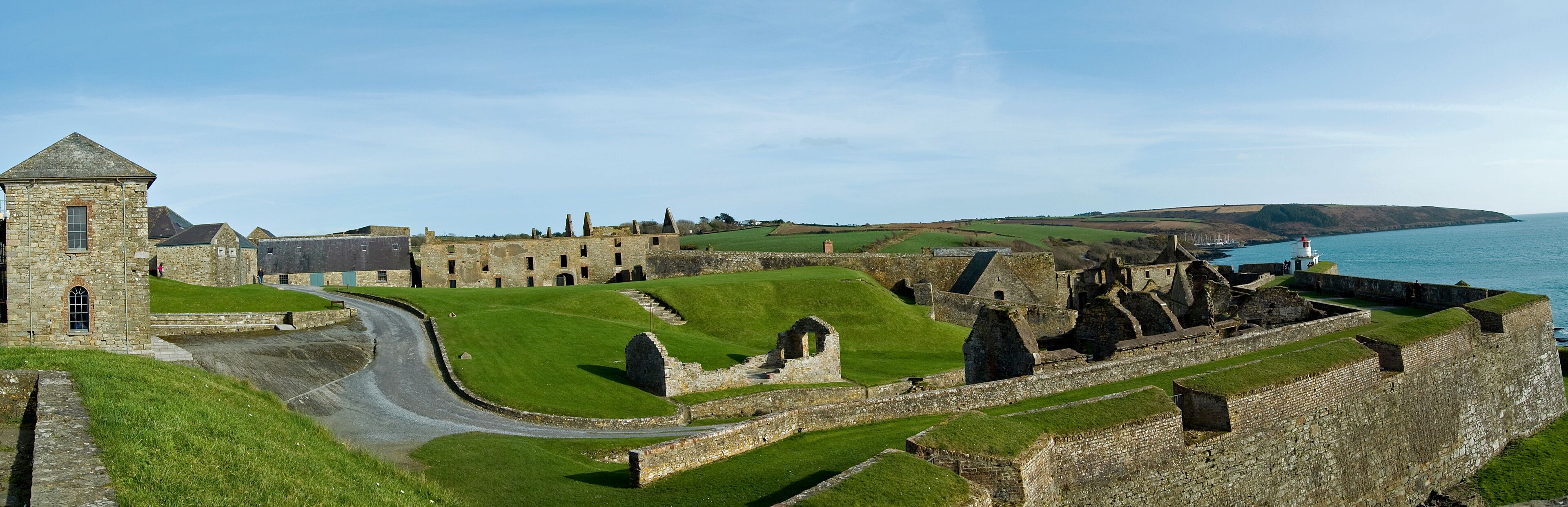 A historic stone castle with a tower, surrounded by green fields and a coastal view.