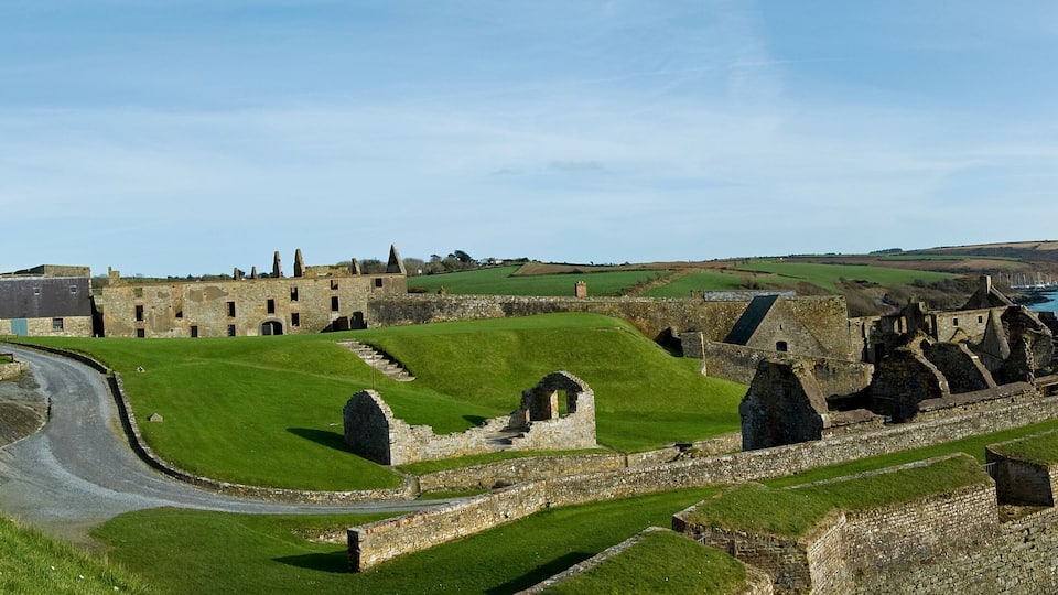 A historic stone castle with a tower, surrounded by green fields and a coastal view.