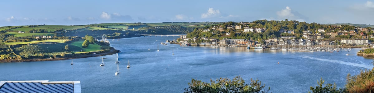 A coastal town with a harbor, sailboats, and rolling green hills.