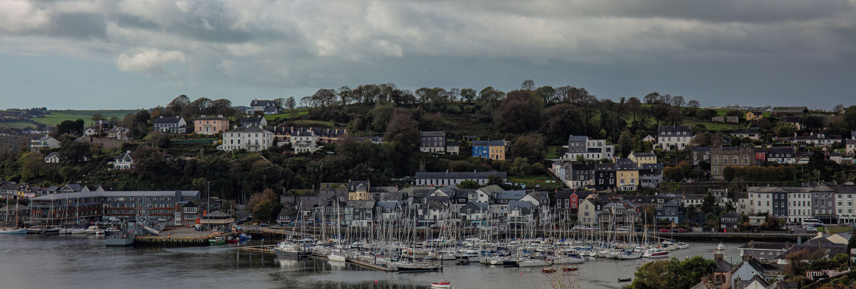 A harbor with numerous boats docked, surrounded by a town with buildings on a hillside.
