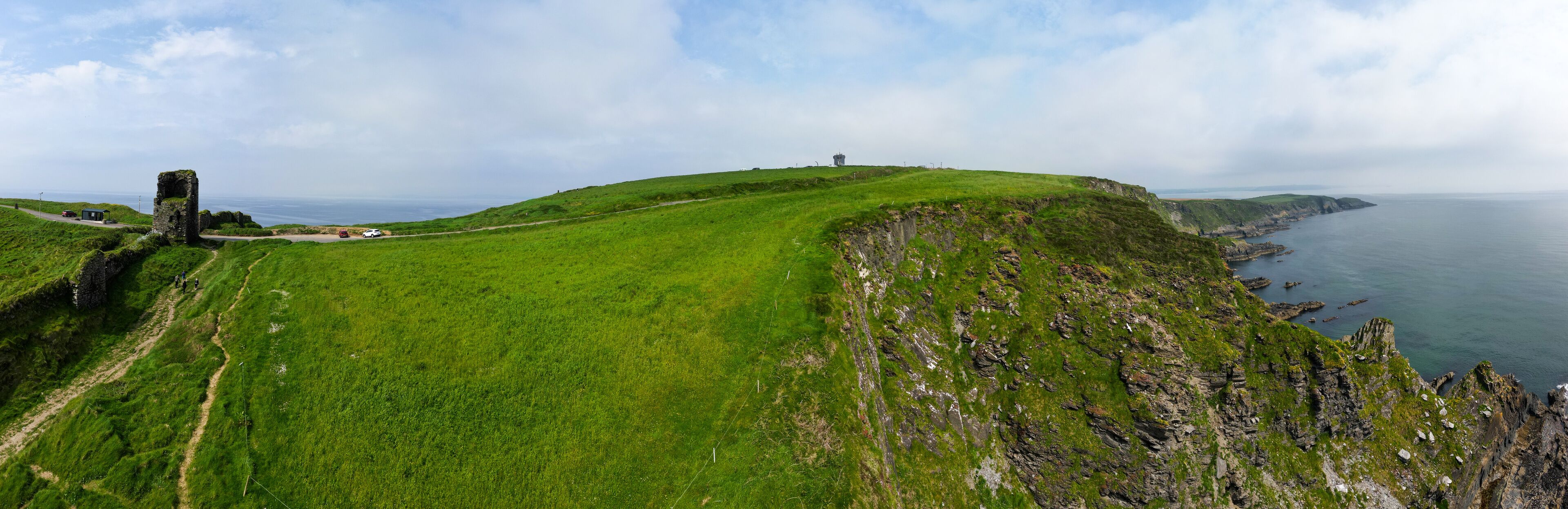 A grassy hill with a stone structure and a coastal view.