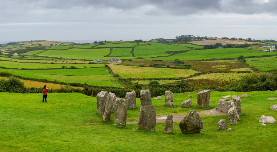 Un círculo de piedras en un campo verde exuberante, con colinas onduladas al fondo.