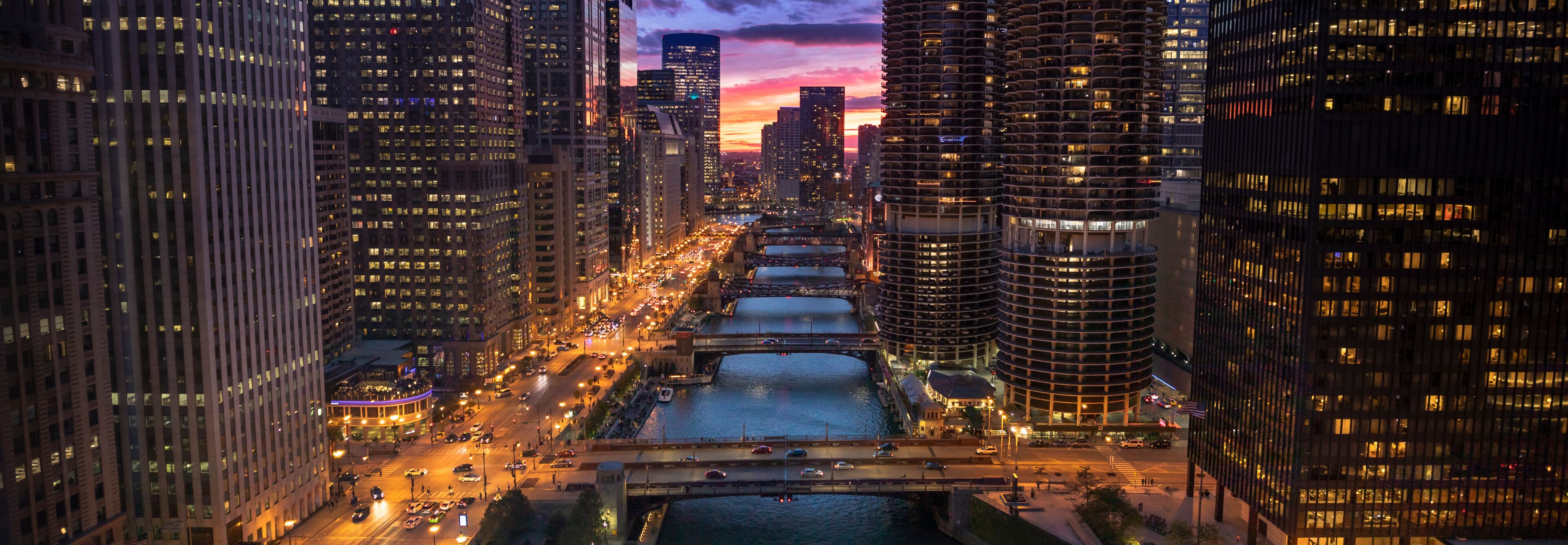 A cityscape with tall buildings, a river, and a bridge at dusk.