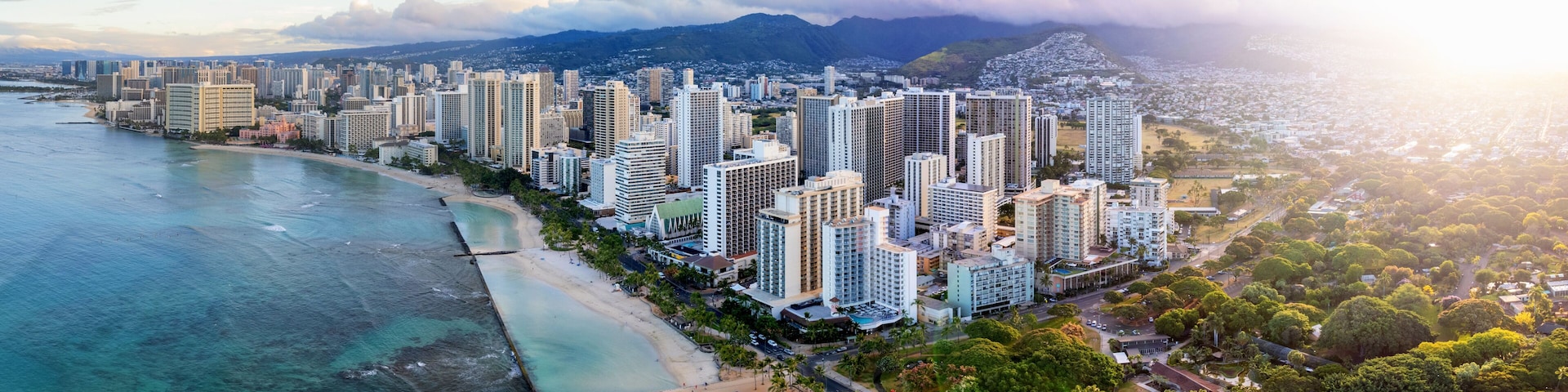 Paisagem costeira com edifícios altos, uma praia e montanhas ao fundo.