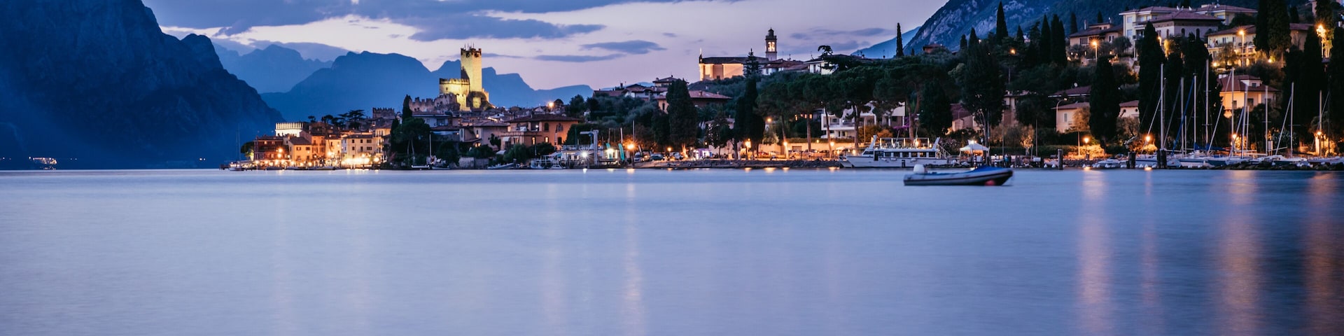 A calm lake with a town on the shore, mountains in the background, and boats in the water.