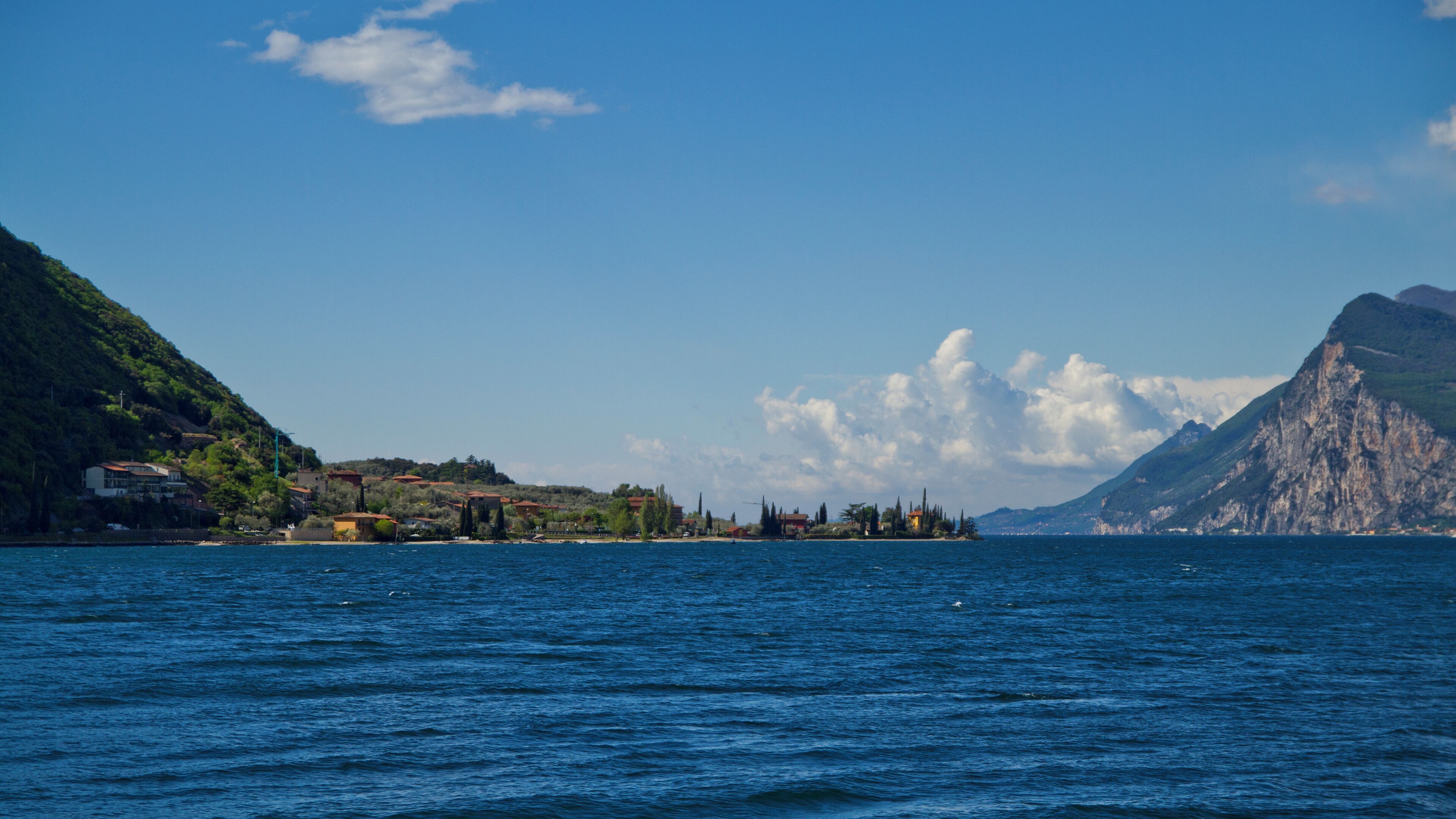 A coastal landscape with a clear blue sea, a small island with buildings, and a mountain in the background.