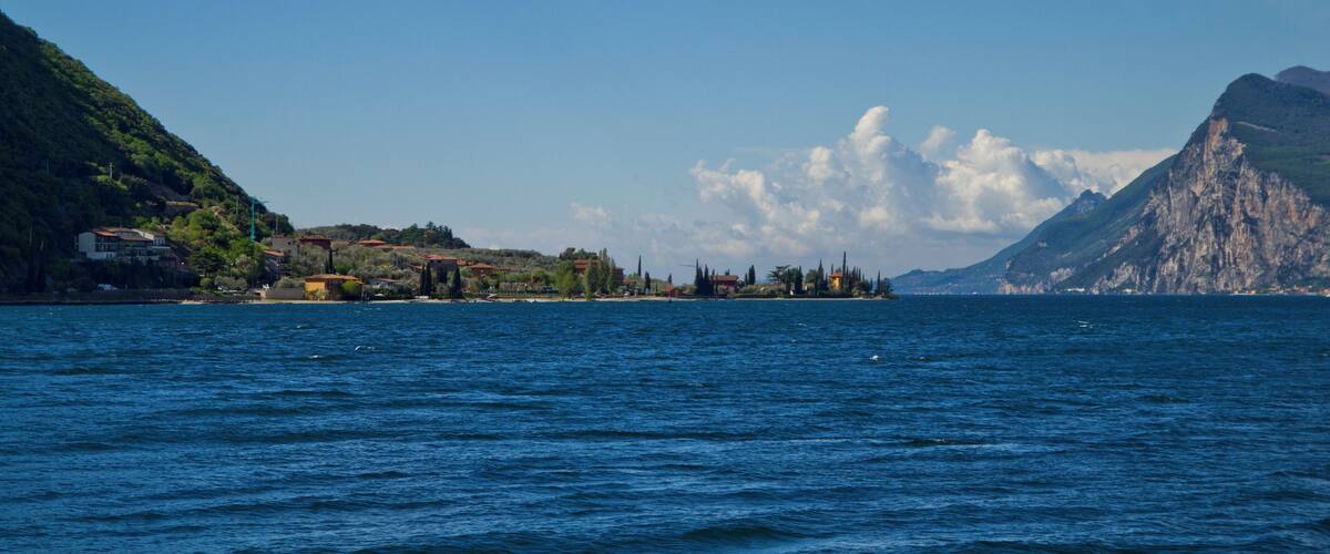 A coastal landscape with a clear blue sea, a small island with buildings, and a mountain in the background.