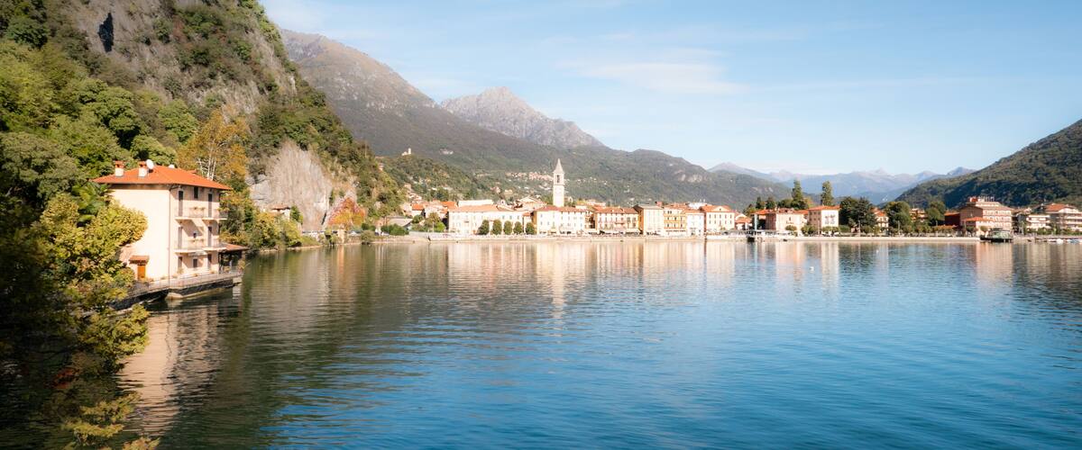 A lake with buildings on the shore, a mountain in the background, and a bridge connecting the buildings to the shore.