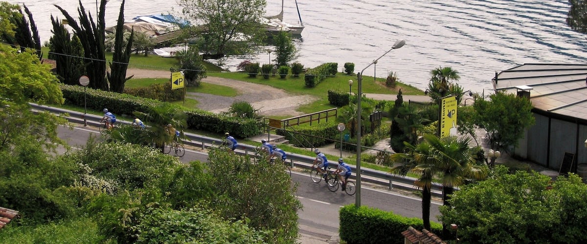 A lake with a sailboat, cyclists on a path, and greenery.