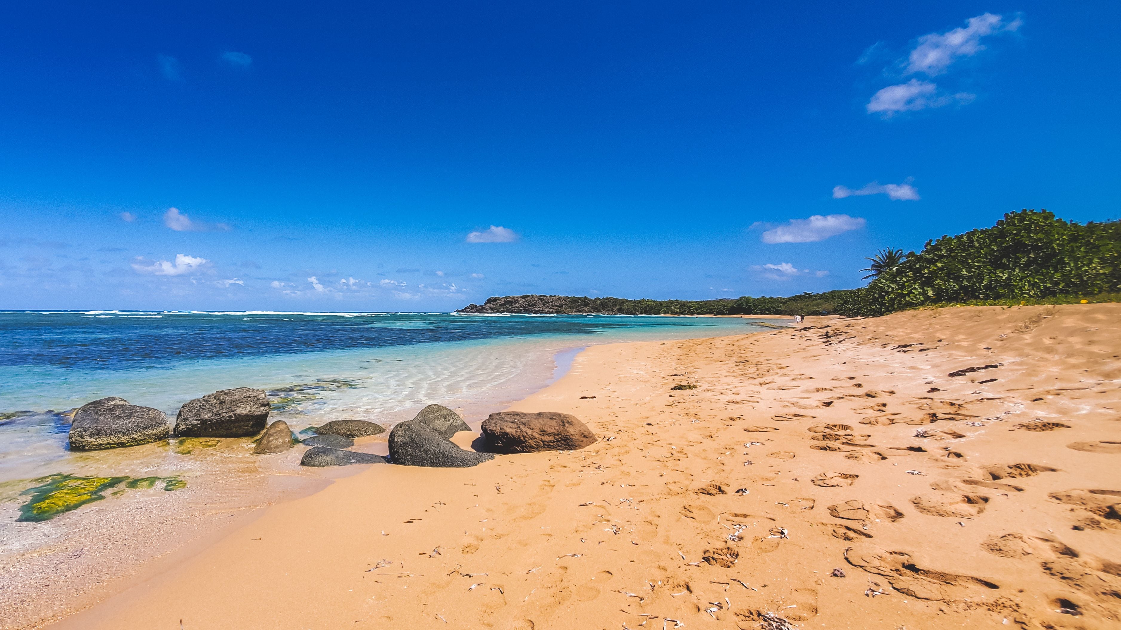 A tropical beach with clear turquoise waters, large rocks in the sand, and a distant island.