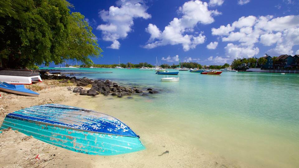 A beach with boats, clear turquoise water, and a rocky shoreline.