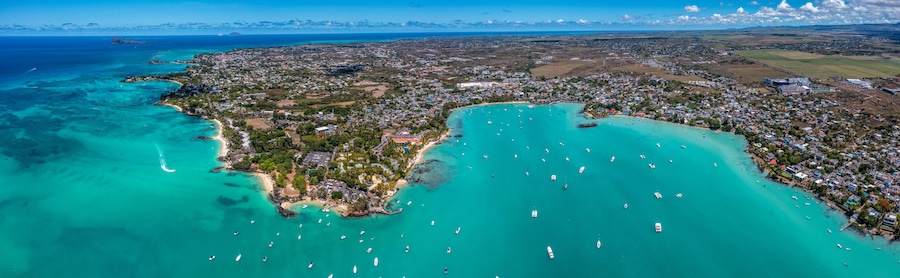 Vista aérea de un pueblo costero con aguas turquesas cristalinas, una zona densamente poblada y una gran bahía con numerosos barcos.