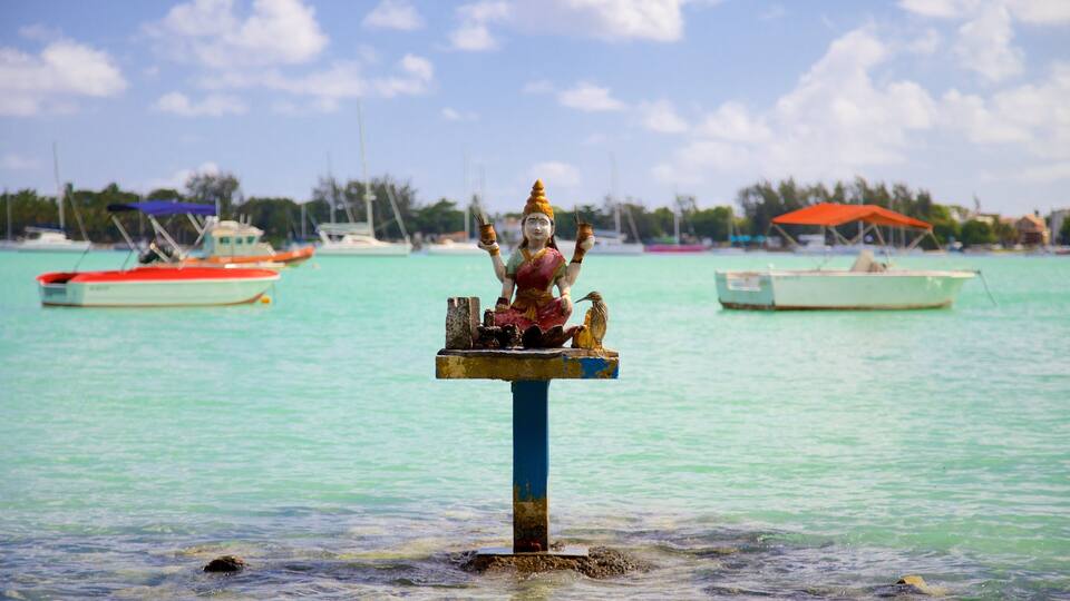 A statue of a deity on a pedestal in the water, surrounded by boats and a clear sky.