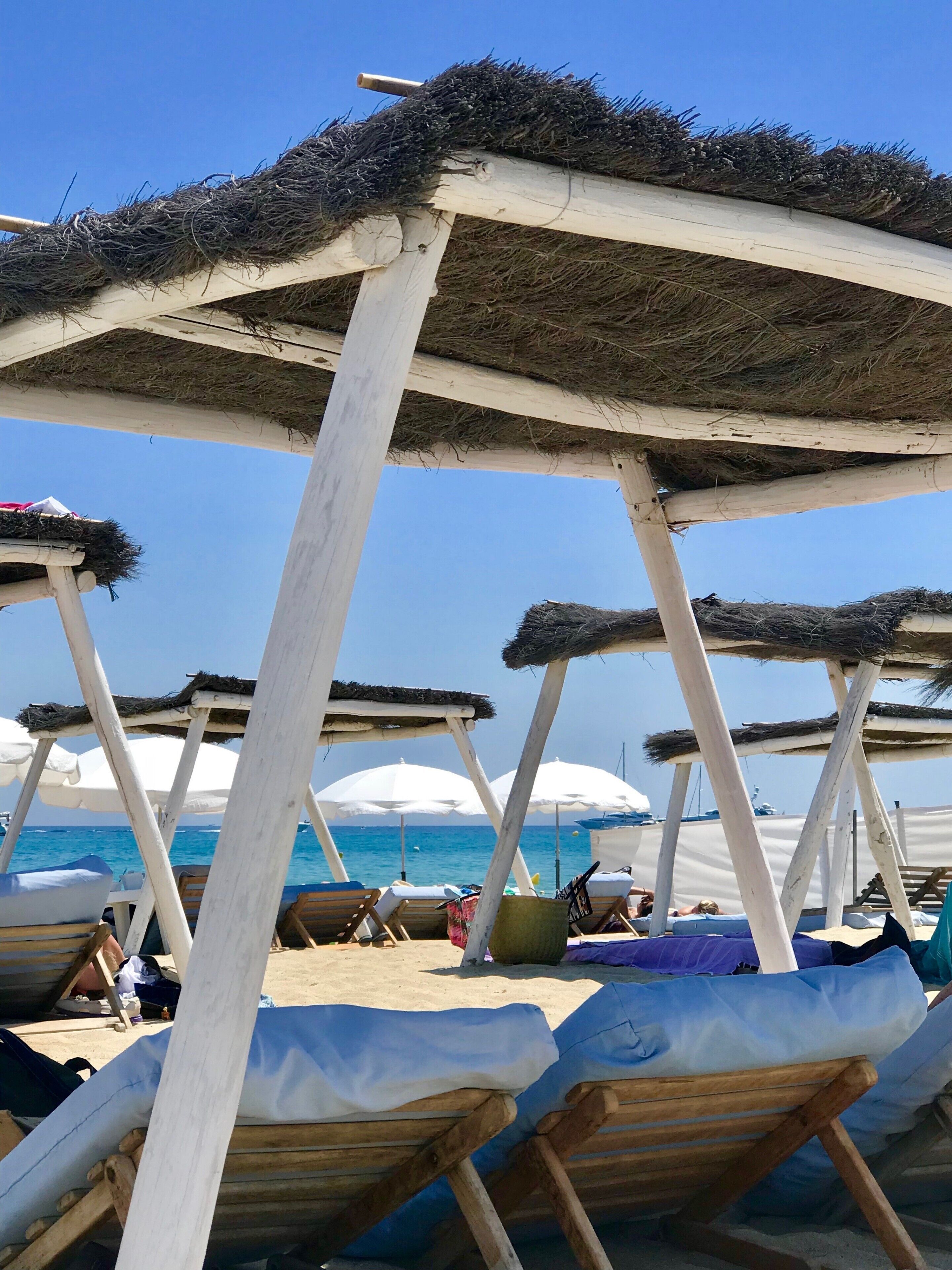Sombrillas y sillas de playa bajo una estructura de madera con techos de paja.