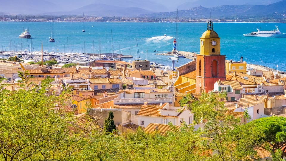 A coastal town with a prominent tower, boats, and a clear blue sea.