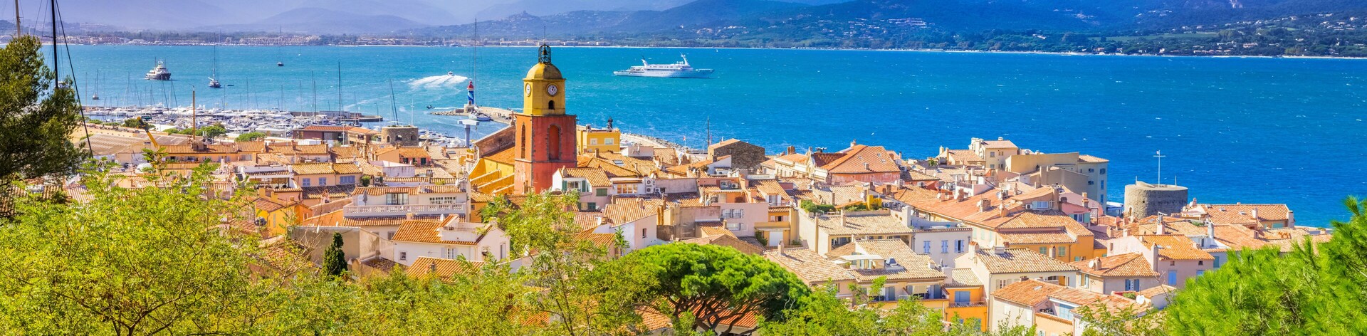 Un pueblo costero con una torre destacada, barcos y un mar azul y transparente.